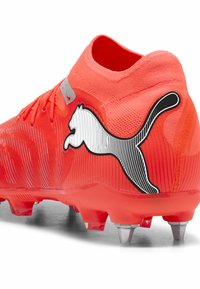 Czerwony syntetyczny but piłkarski z teksturowaną powierzchnią, kołnierzem przypominającym skarpetę oraz wyraźnym czarno-białym logo Puma po boku.