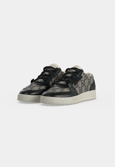 Paire de baskets basses en tissu beige à motifs avec des détails en cuir noir, des lacets noirs et des semelles épaisses en caoutchouc clair.
