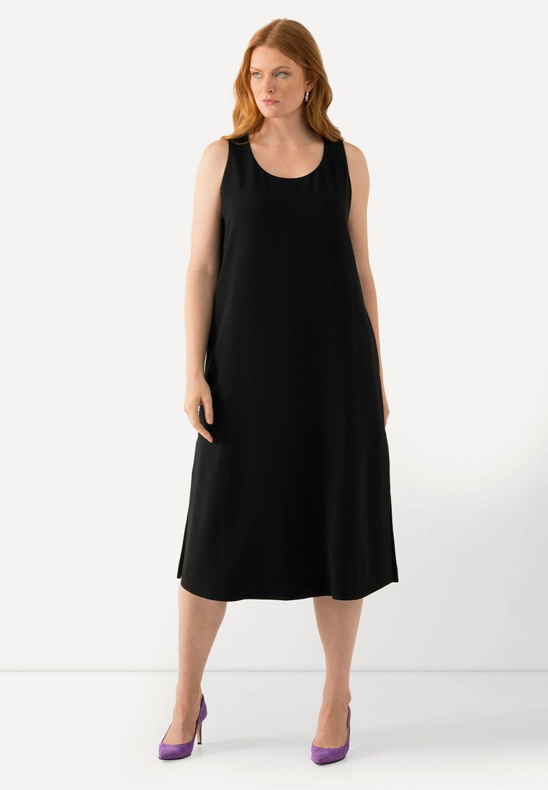 Vestido negro sin mangas con un escote redondeado, diseñado con una silueta fluida. Llevado con tacones altos morados, que presentan una textura suave.