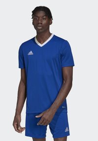 Blå idrettsjakke med hvit V-hals, korte ermer og Adidas-logo på venstre bryst. Kombinert med matchende blå shorts.