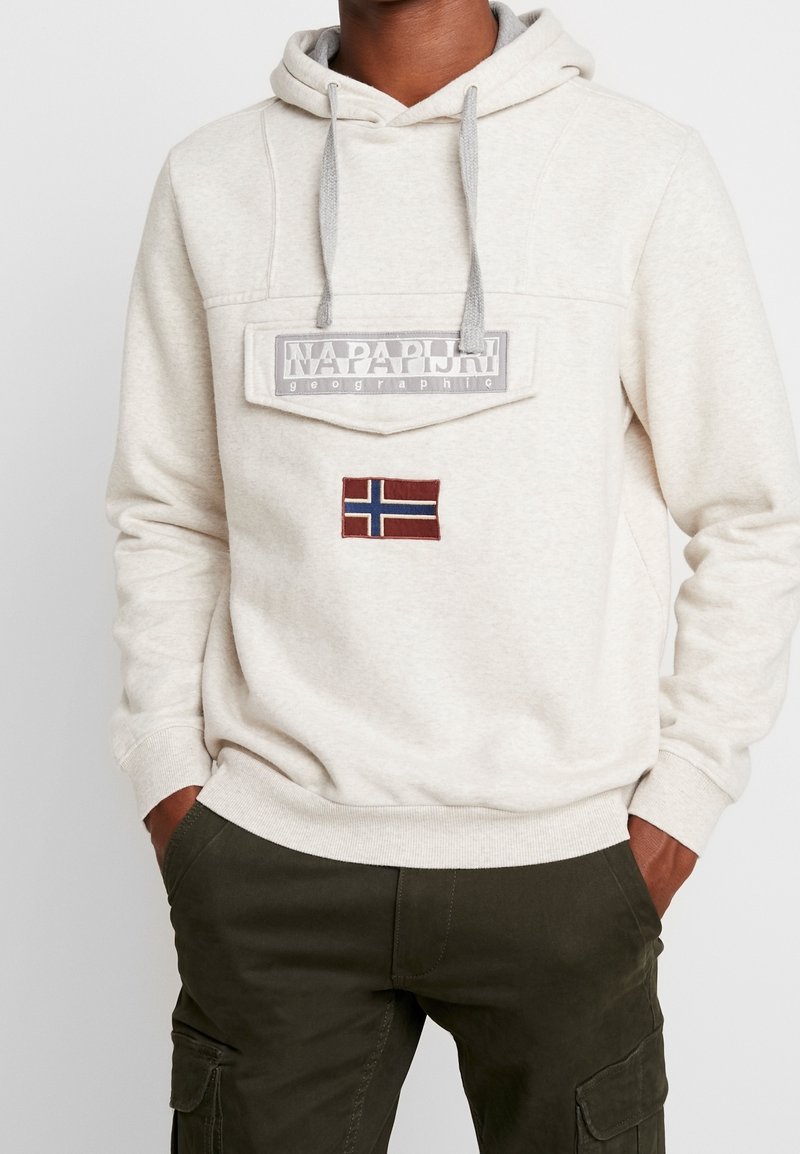 Sudadera color beige con un bolsillo frontal, cordones grises y una bandera de Noruega bordada. El material parece suave y cómodo.