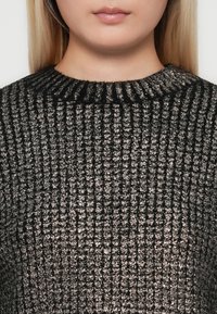 Moteris su tiesiais blondiniais plaukais, dėvinti juodai pilką šilką, atidengiančiu kaklą ir viršutinę krūtinės dalį.