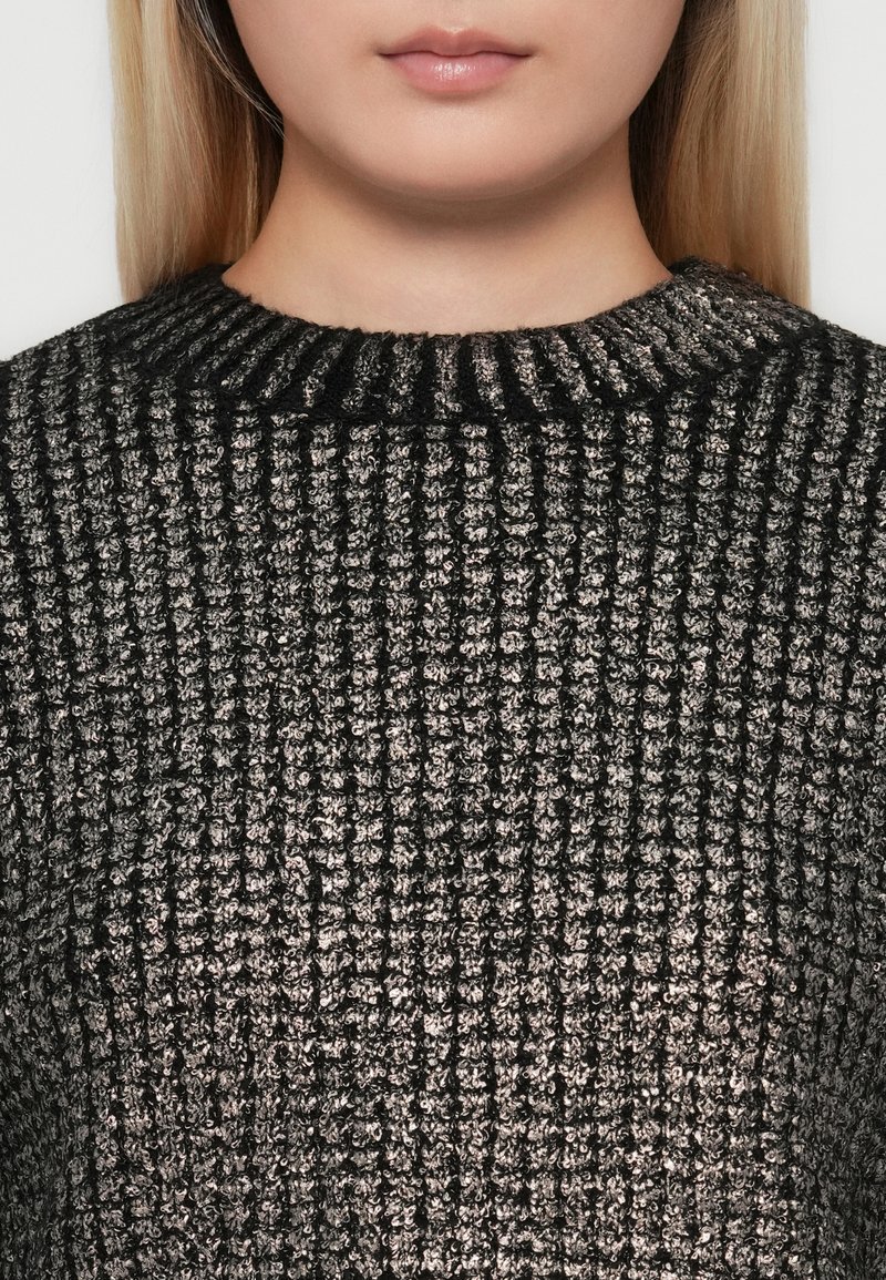 Donna con capelli biondi lisci che indossa un maglione a coste nero e grigio, che mostra il collo e la parte superiore del torace.