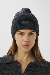 Caciula din tricot ribbed gri închis, cu un vârf conic și un logo subtil embosat pe față, purtată cu un pulover cu guler gri asortat.