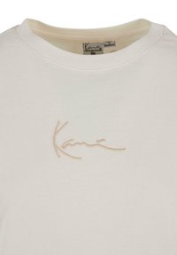 Crèfærvet bomulds t-shirt med rund hals og et broderet beige signaturlogo på brystet. Glat tekstur, afslappet design.