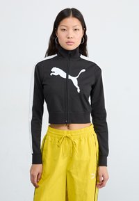 Black cropped zip jacket with high collar and white Puma logo, featuring white side stripes. Paired with yellow drawstring pants.