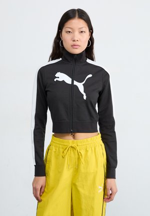 Black cropped zip jacket with high collar and white Puma logo, featuring white side stripes. Paired with yellow drawstring pants.