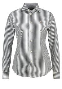 Gestreifte Hemdbluse in Marineblau und Weiß mit klassischem Kragen, langen Ärmeln und einem kleinen Emblem auf der Brust. Aus Baumwollmaterial.