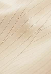 Gros plan sur un tissu beige avec de fines coutures diagonales créant un motif géométrique subtil et une surface texturée.
