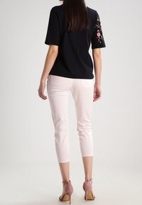 Top nero a maniche corte con ricami floreali sulla spalla destra, abbinato a pantaloni fitted rosa chiaro e sandali con tacco rosa.