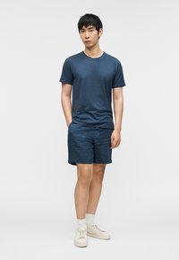 Σκούρο μπλε βαμβακερό T-shirt και ταιριαστά σορτς, με στρογγυλή λαιμόκοψη, κοντά μανίκια και άνετη εφαρμογή. Συνδυασμένα με λευκά αθλητικά παπούτσια και κάλτσες.