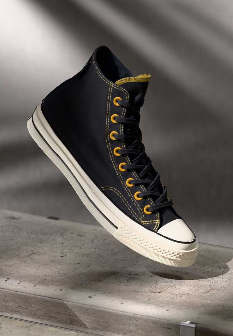 Zapatillas altas de lona azul marino con ojales y costuras amarillas, puntera de goma blanca y suela texturizada blanca.