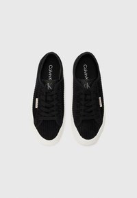 Black corduroy sneakers with a textured surface, white rubber sole, and black laces. Features Calvin Klein branding on the insole and side tag.