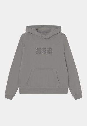 Felpa grigia con cappuccio e tasca frontale. Presenta il logo "Calvin Klein Jeans" in un grigio più scuro, polsini e orlo a costine. Tessuto morbido.
