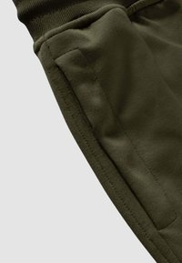 Primo piano della tasca di pantaloni verde oliva con cuciture visibili e bordo della cintura elastica a coste.