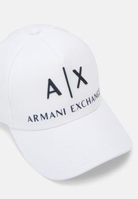 Hvit baseballcaps med avrundet krone, prydet med mørkeblå brodert logo "A|X" og "ARMANI EXCHANGE" på fronten.