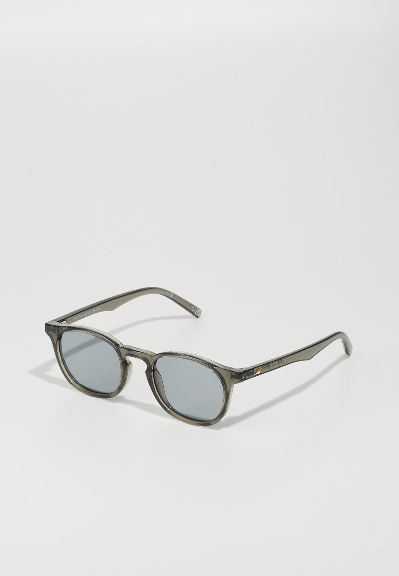 Ochelari de soare cu nuanță gri, cu lentile rotunde și o ramă gri translucidă. Prezintă brațe subțiri, elegante, cu detalii minime de accent.