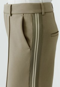 Maßgeschneiderte Hose aus hellbraunem Material mit glatter Textur, ausgestattet mit Seitentaschen und vertikalen Streifenakzenten in gedämpftem Grün und Creme.