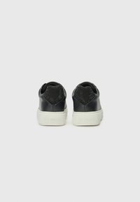 Zwarte leren sneakers met witte rubberen zolen, voorzien van een textiel zwarte stof bij de hiel en een reliëflogo-detail aan de zijkanten.