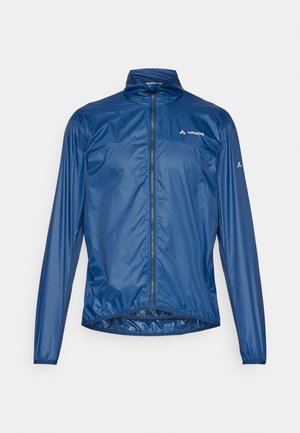 Granatowa, lekka kurtka z wysokim kołnierzem, pełnym zamkiem z przodu i elastycznymi mankietami. Posiada odblaskowe logo oraz miękką, gładką teksturę.