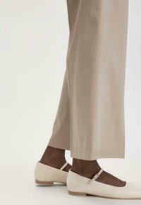 Beige wijde broek gemaakt van een soepele stof, gecombineerd met crèmekleurige ballerina's met een gespsluiting en een lage houten hak.