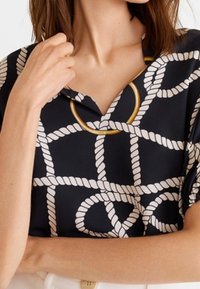 Blusa navy con motivo a corda bianco, con un accento circolare dorato in prossimità del collo e una vestibilità rilassata. Tessuto morbido.