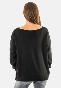 Suéter negro de gran tamaño con un escote amplio, mangas largas y puños de canalé. La tela parece suave con una textura ligeramente peluda.