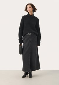 Černý pletený svetr s vysokým límcem, doplněný dlouhou černou džínovou sukní. Outfit zahrnuje černý opasek a černé kotníkové boty na podpatku.