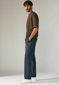 Camiseta marrón de manga corta combinada con pantalones de color azul oscuro y zapatillas blancas. La tela parece suave y tiene un ajuste relajado.