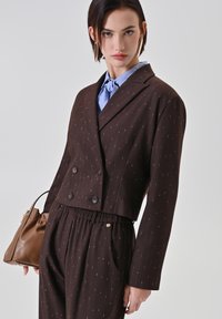 Brauner zweireihiger Blazer mit kurzem Schnitt, versehen mit dezenten weißen Nadelstreifen, kombiniert mit passenden, hoch taillierten Hosen und einer blauen Bluse.