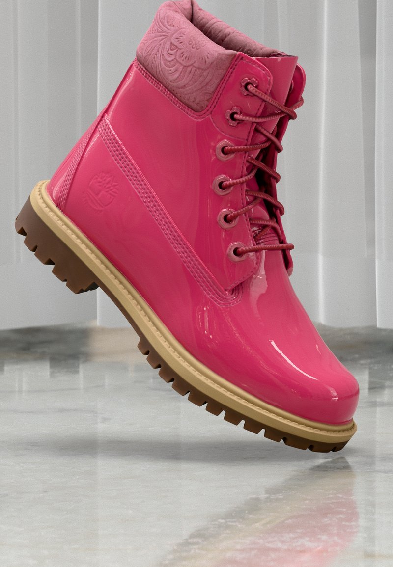 Botas impermeáveis cor-de-rosa com um acabamento brilhante, colarinho texturizado em rosa e sola exterior robusta em castanho. Apresenta seis orifícios para os atacadores e um logótipo.