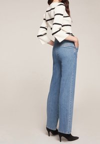 Vit ribbad tröja med svarta ränder, kombinerad med högmidjade ljusblå vida jeans och svarta högklackade stövlar.