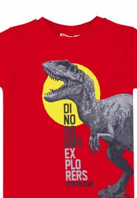 Červené tričko s šedou grafikou dinosaura na žlutém pozadí kruhu. Text zní "OFICIÁLNÍ KLUB PRŮZKUMNÍKŮ DINOSAURŮ."