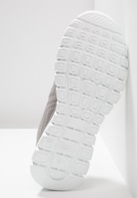 Graue, netzartige Sportschuhe mit einer weißen strukturierten Gummisohle, die ein Gittermuster und eingesenkte Quadrate für besseren Grip aufweist.