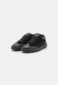 Sneakers neri con una combinazione di pelle e suede, punta rotonda, suola piatta e un logo prominente impresso di lato.