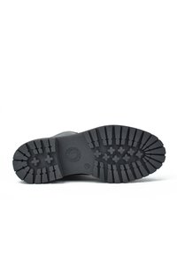 Suela de bota de goma negra con un patrón de huella texturizado, que presenta surcos profundos y un logo circular en el centro.