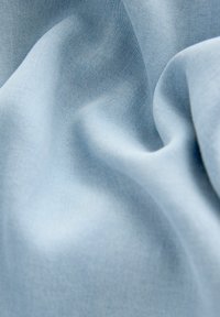 Tissu bleu clair avec une texture lisse, présentant de fines trames diagonales et un éclat subtil, drapé doucement pour créer des formes fluides.