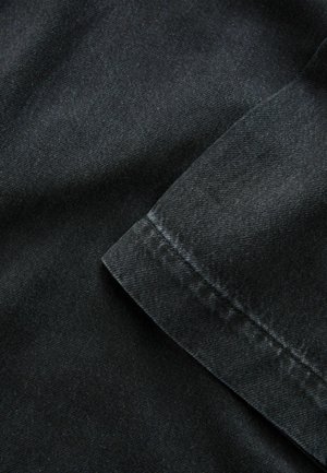 Tissu en denim noir avec une texture lisse, présentant un bord replié et des coutures visibles, mettant en avant sa construction robuste.