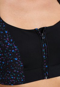 Top sportivo nero con zip frontale, caratterizzato da un pannello nero testurizzato con spruzzate multicolori in viola, verde acqua e azzurro chiaro.