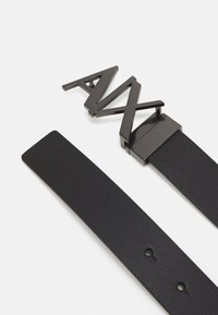 Black leather belt featuring a textured strap and a bold, angular metallic buckle with the letters "AMX" in a matte finish.