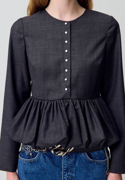 Top peplum grigio scuro con maniche lunghe, dotato di scollatura rotonda e otto bottoni decorativi lungo il davanti. Tessuto con texture e vita arricciata.
