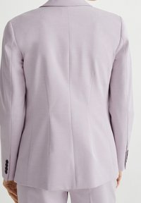 Jasnolawendowy żakiet o dopasowanym kroju, z długimi rękawami, klapami i trzema czarnymi guzikami na każdym mankiecie. Posiada gładką fakturę oraz szwy z tyłu.