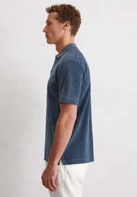 Donkerblauwe polo met korte mouwen, gemaakt van zachte stof, met een geribbelde kraag en zijsplitten voor gemakkelijke beweging. Minimalistisch ontwerp.