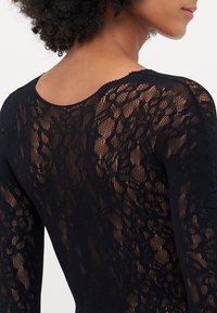Body nero in pizzo con un design testurizzato, scollatura rotonda e maniche lunghe, che mette in mostra motivi intricati e tessuto trasparente.