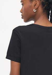 Svart bomulls t-skjorte med rund hals, rullet korte ermer og glatt tekstur. Ingen synlige mønstre eller logoer. Enkelt design.