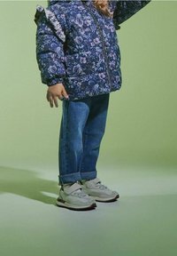 Blumige Daunenjacke in Marineblau, Jeans im Denim-Look und hellgraue Sneaker mit Klettverschluss und Gummi-Sohlen. Strukturierter Stoff mit Rüschensämlen.
