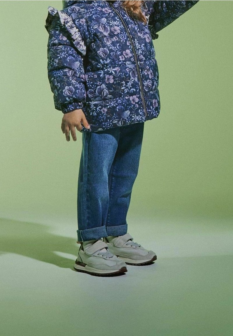 Blumige Daunenjacke in Marineblau, Jeans im Denim-Look und hellgraue Sneaker mit Klettverschluss und Gummi-Sohlen. Strukturierter Stoff mit Rüschensämlen.