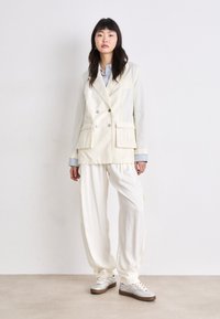 Kremfarget dobbeltspent blazer med to frontlommer, kombinert med løse kremfargede bukser og metalliske sølv-sneakers. Lett stoff, skreddersydd design.