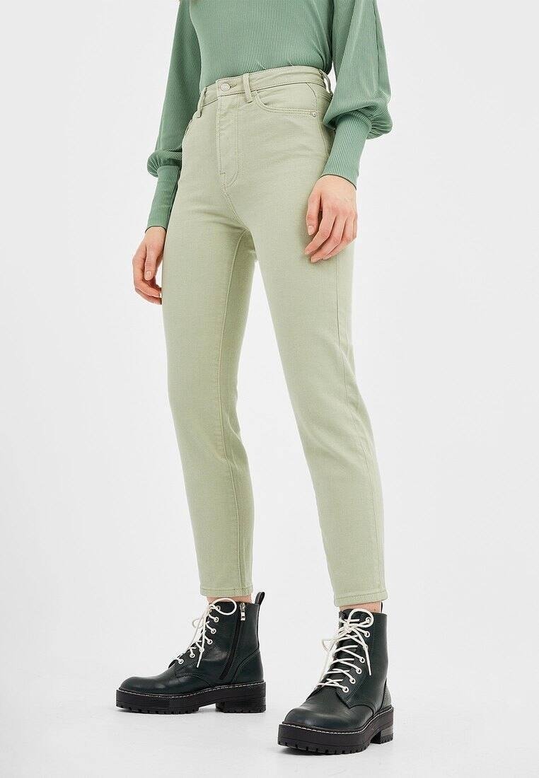 Personne portant un pantalon taille haute vert clair, un haut vert côtelé manches longues et des bottes de combat noires avec des lacets blancs.