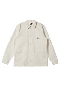 Cream-colored, long-sleeve jacket with a button front, two large front pockets, and a small logo patch on the chest pocket. Cotton material.